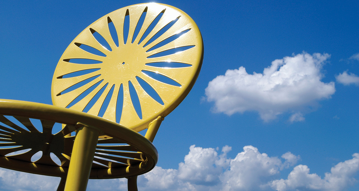 A yellow chair with blue sky and white fluffy clouds in the background