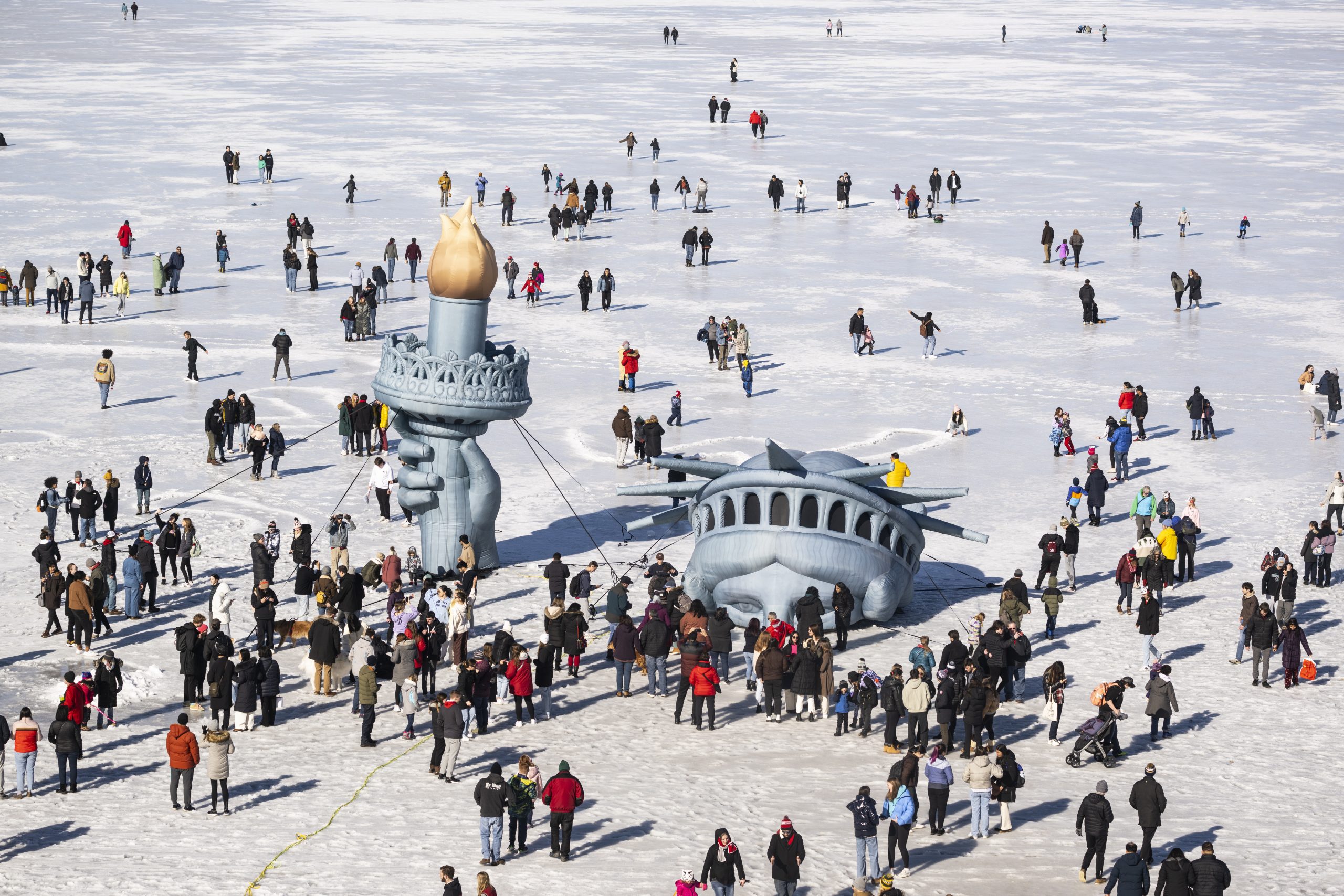 A Statue of Liberty replica on frozen lake surrounded by people
