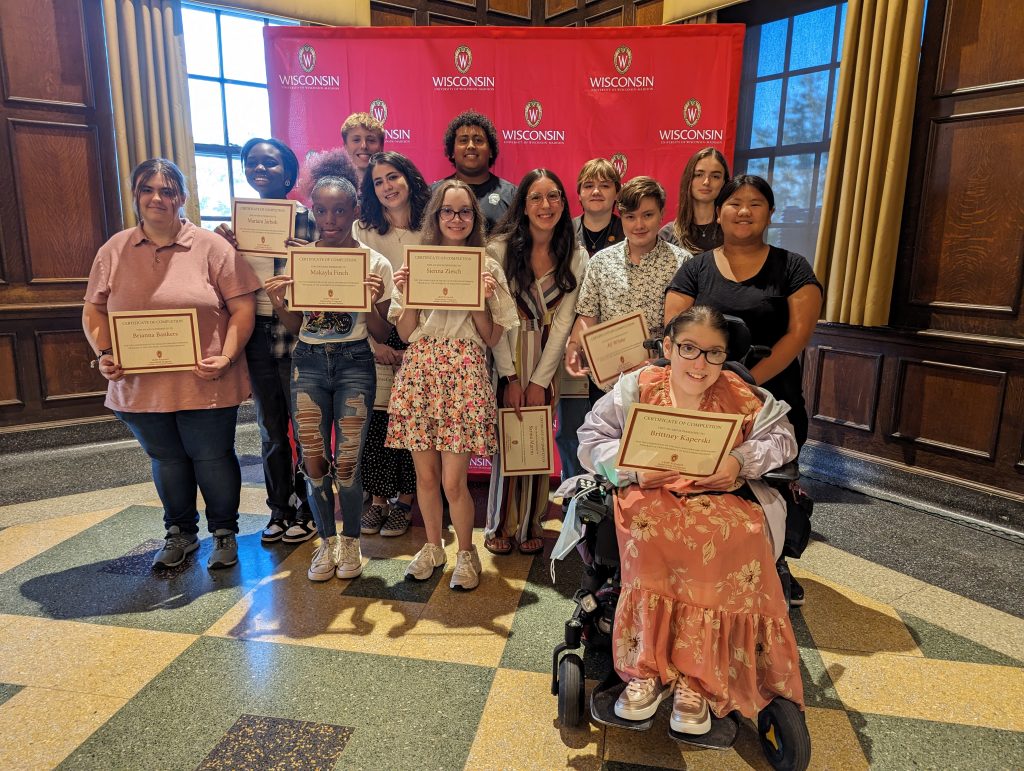 A diverse group of high school students stand together proudly showing their certificates.
