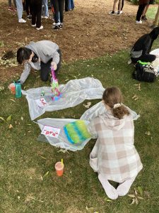 Two students kneel on the grass in front of their tie dying projects.