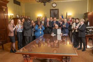 Tony Evers displays a bill he just signed with a group of people behind him clapping.