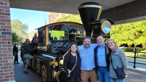 Four people stand in front of a small black train engine