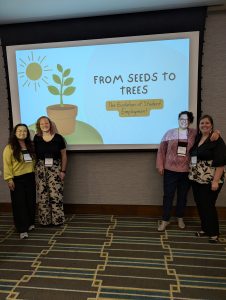 Four women stand in front of a presentation screen, two on each side
