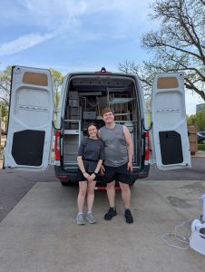 Two students stand in front of an open van that's filled.