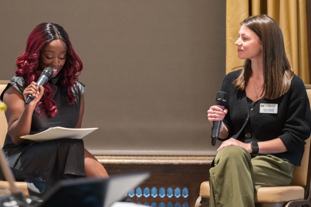 Two women with microphones sitting on a stage.