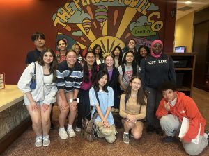 Group photo of students in front of a colorful mural with inspirational words and hot air balloons.