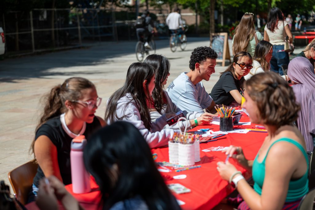 Students sit at a long table outside creating buttons.