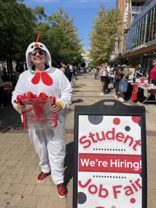 A women in a chicken costumer stands next to the Job Fair sign