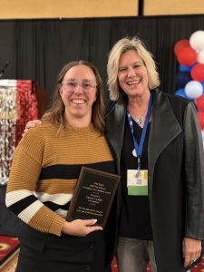 Two people pose, one holding a plaque