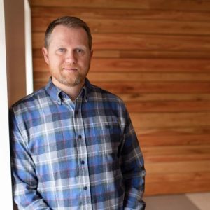 Man in blue shirt leaning against a wall