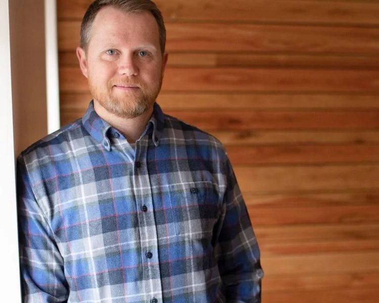 Man in blue shirt leaning against a wall