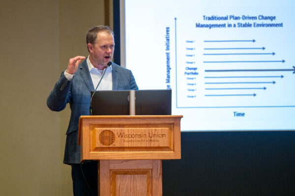 Man speaking at a podium with a presentation on a screen behind him